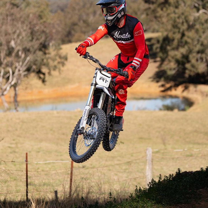 Rider jumping a Rerode electric dirt bike on a rural property